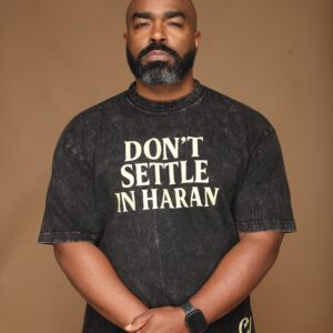Man wearing a black shirt with 'DON'T SETTLE IN HARAN' text.