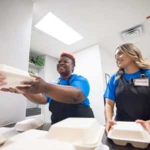 Two food service workers handing out takeout containers.