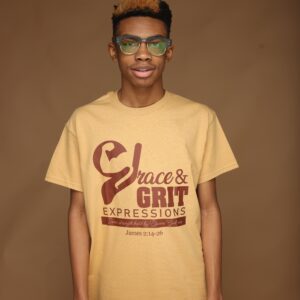Young man wearing glasses and a beige graphic t-shirt against a brown backdrop.