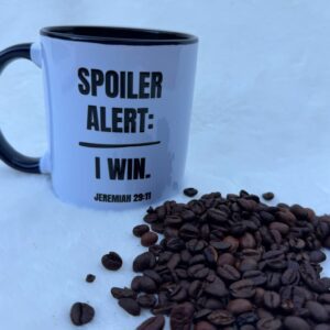 Coffee mug with a witty 'Spoiler Alert: I Win' quote and coffee beans scattered.