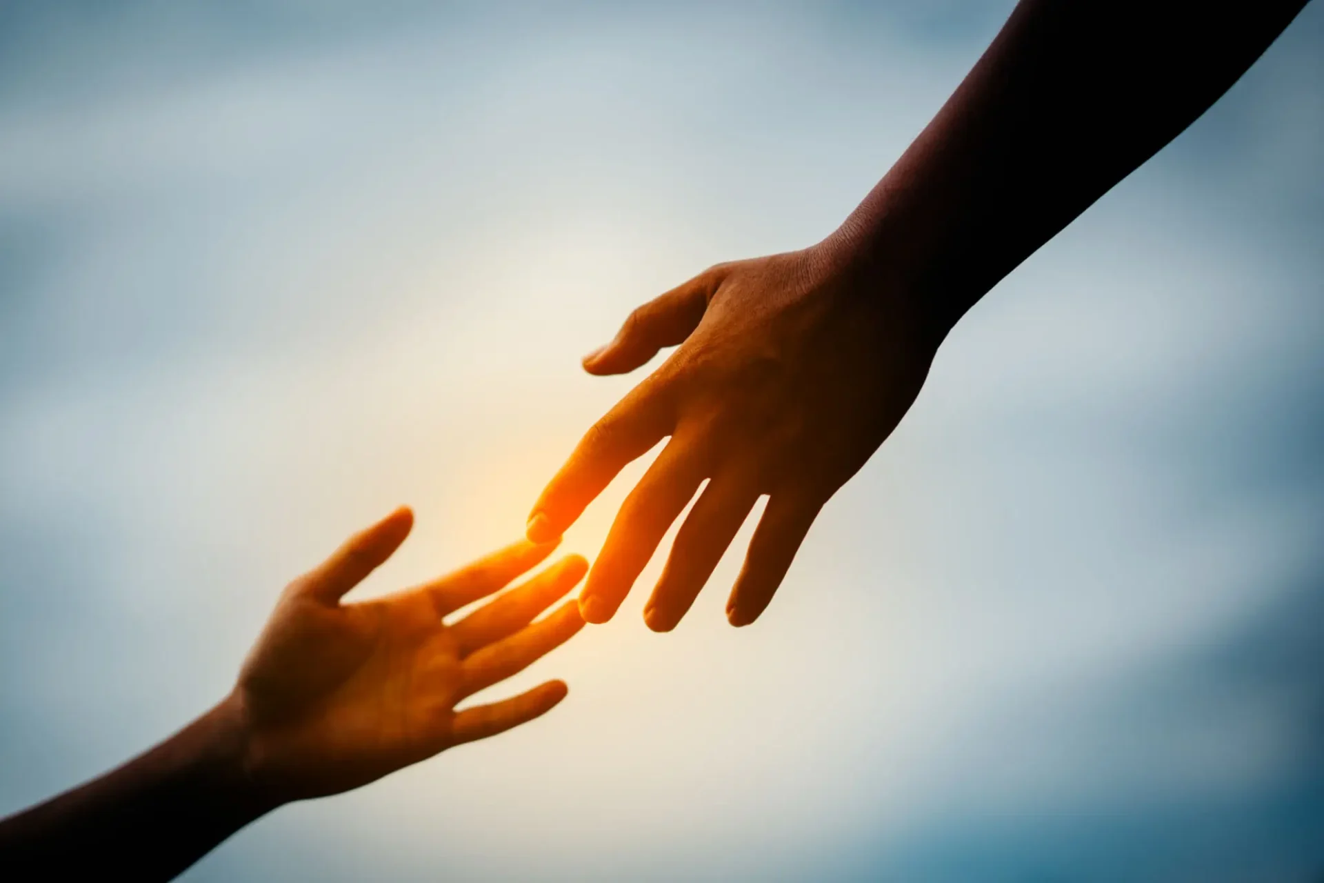 Two hands reaching out toward each other with sunlight in the background.