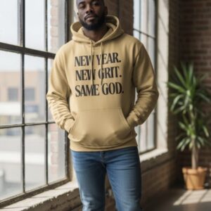 Man in a beige hoodie with inspirational text, standing by a window.