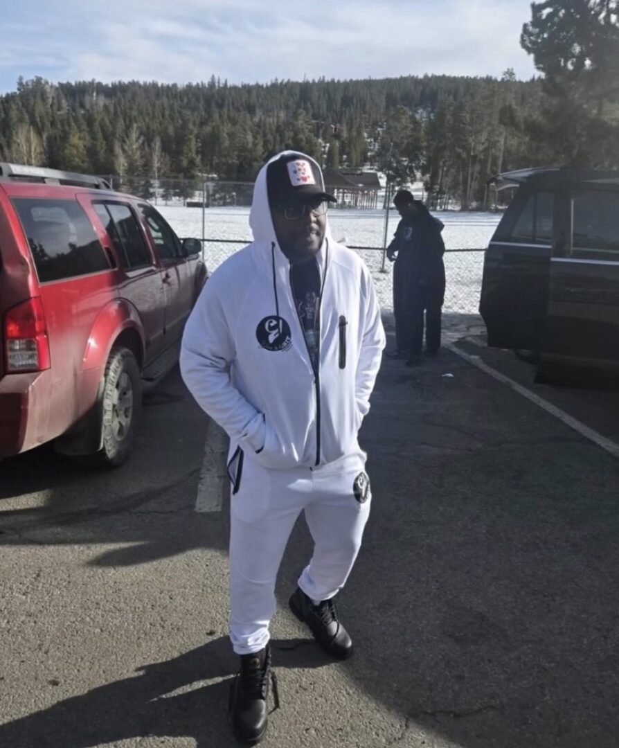 Person dressed in white tracksuit and mask standing in a parking lot.