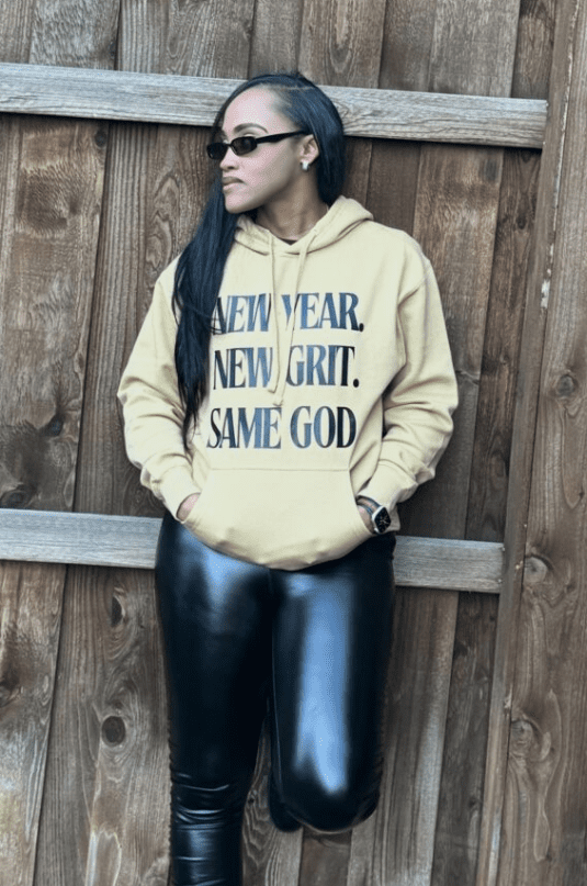 Person wearing a yellow hoodie with text and shiny black pants.