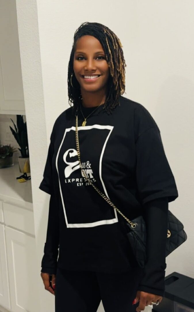 Smiling woman wearing a black oversized graphic t-shirt and carrying a black purse.